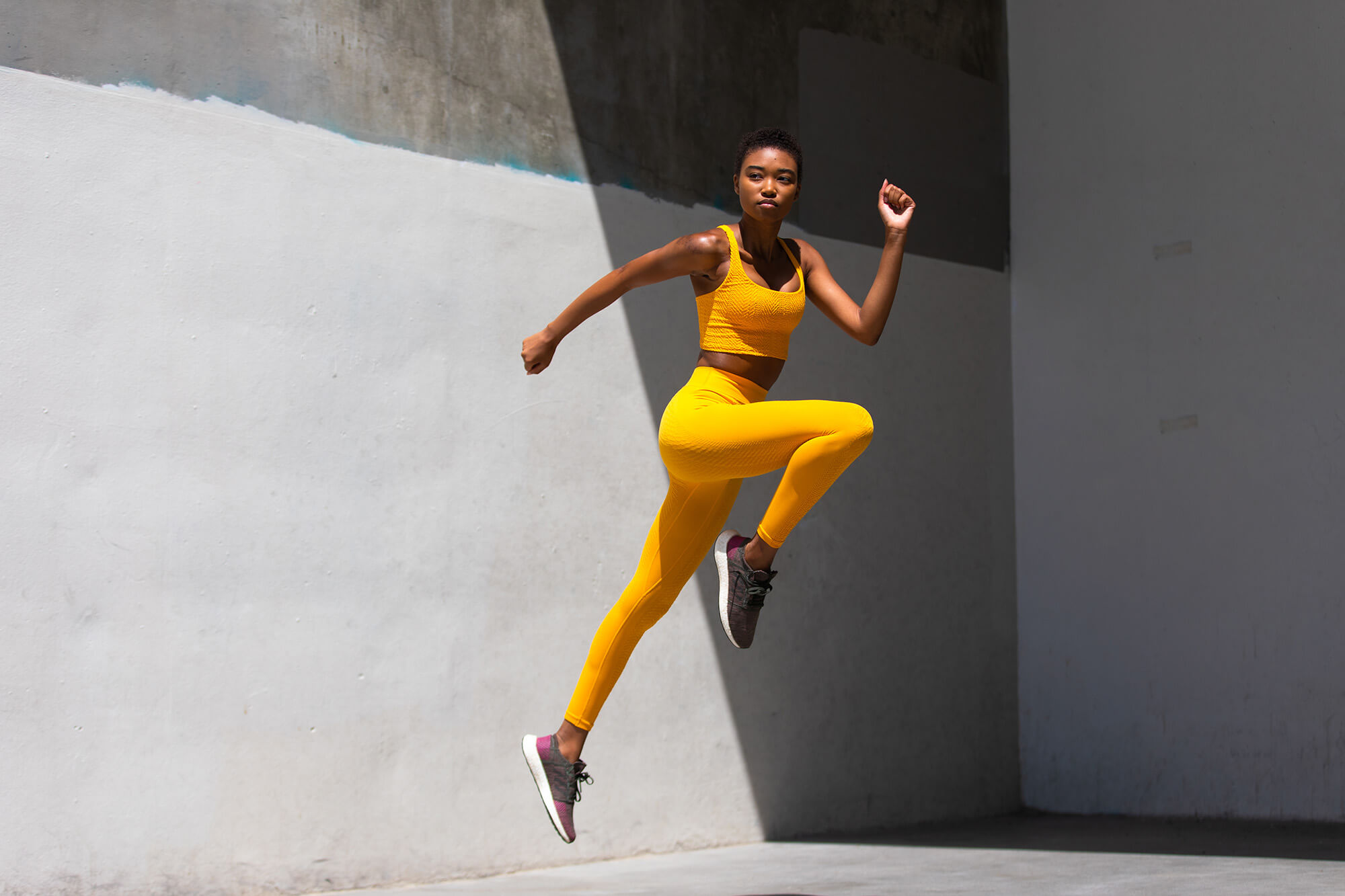 Women in yellow athletic cloths, showing a squat jump. Captured by fitness photographer cameron michael